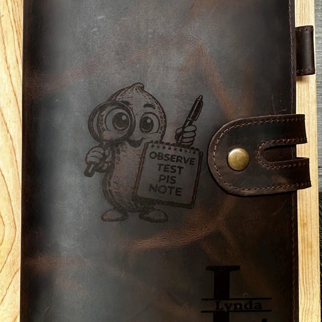 Customer photo: dark brown leather journal engraved with a custom illustration and an L monogram
